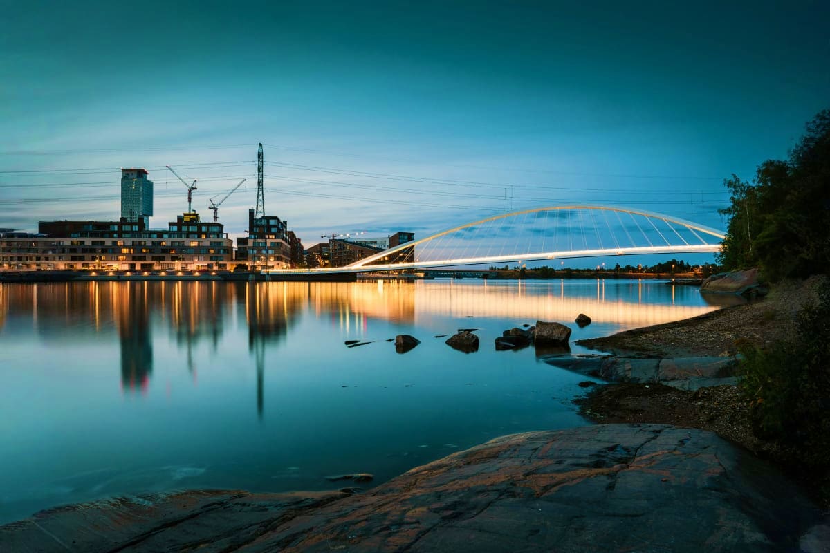 Illuminated bridge and buildings reflecting in calm water at dusk in Helsinki, Finland