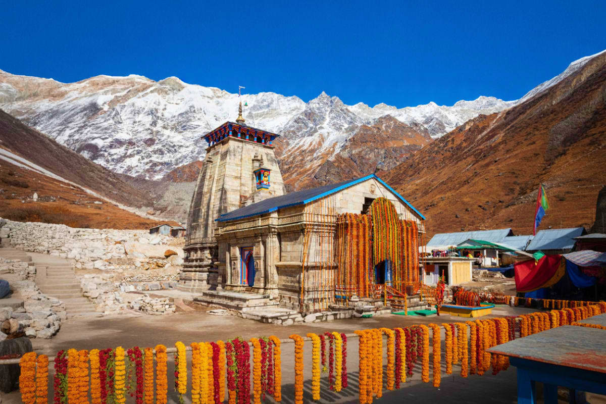 Kedarnath Temple with snow-capped Himalayan peaks, colorful marigold garlands, and devotional decorations in the sacred valle