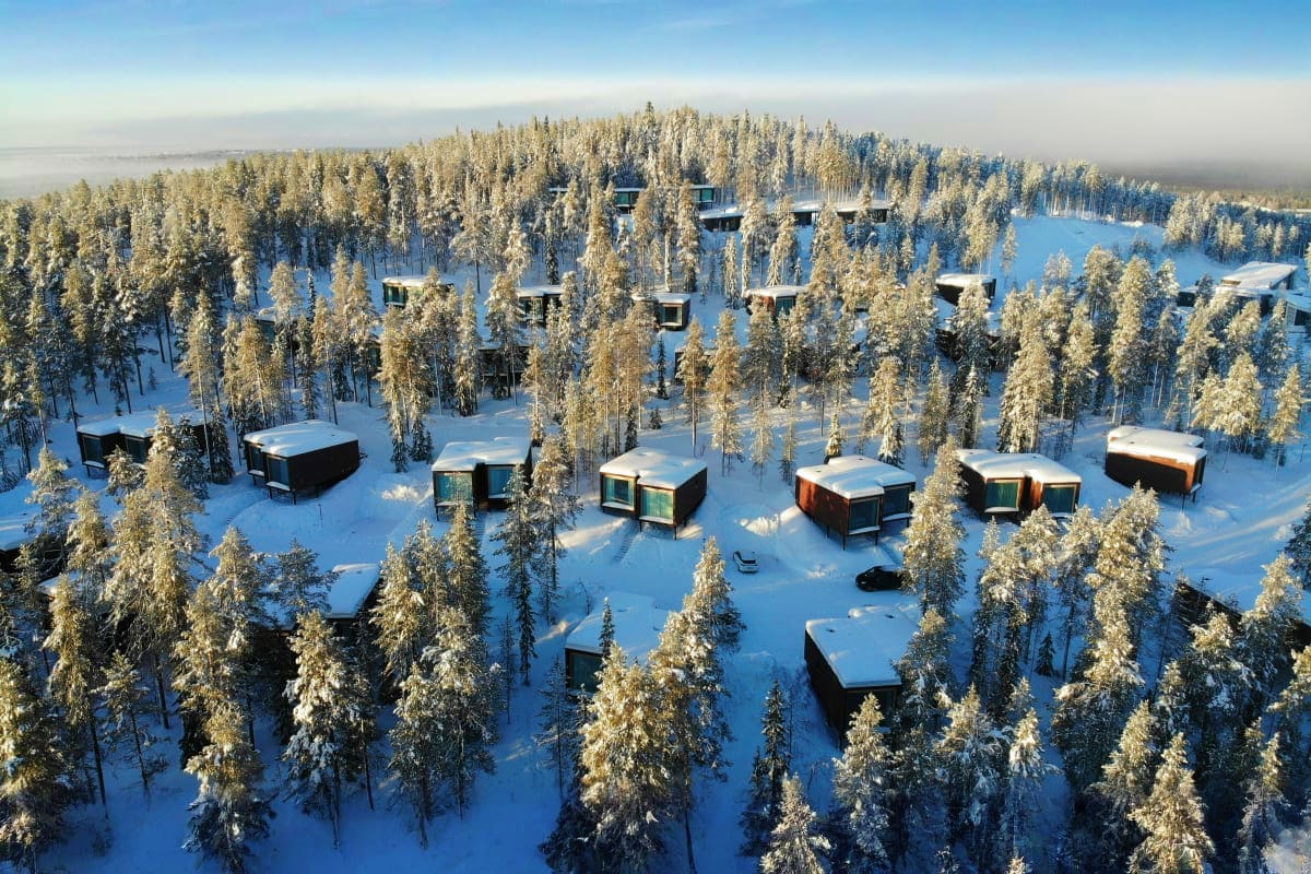 Aerial view of modern glass cabins scattered among snow-covered pine forest in Finnish Lapland during winter