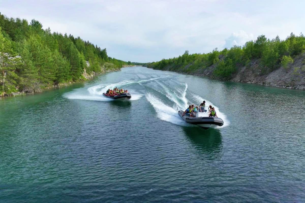 Two speedboats with passengers racing across turquoise river surrounded by dense evergreen forests in Estonia