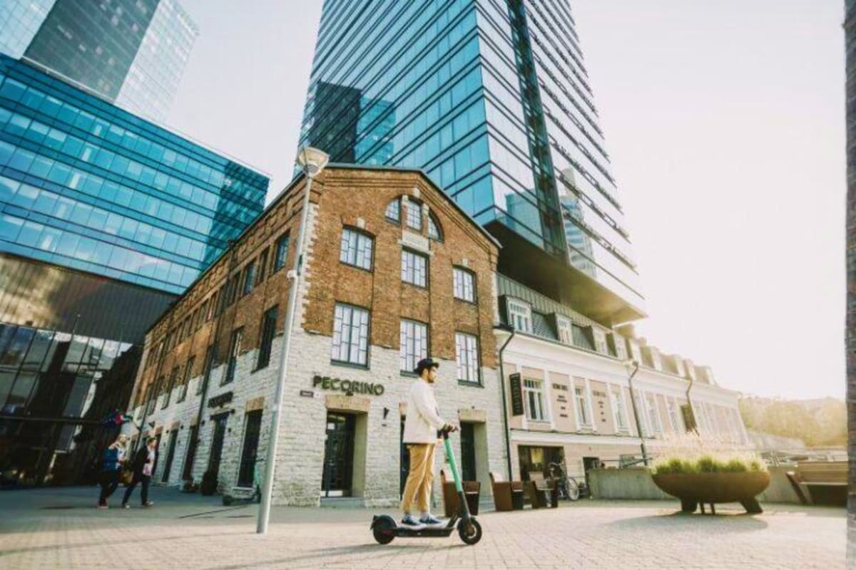 Historic brick building with Pecorino storefront surrounded by modern glass towers, person on electric scooter in foreground,