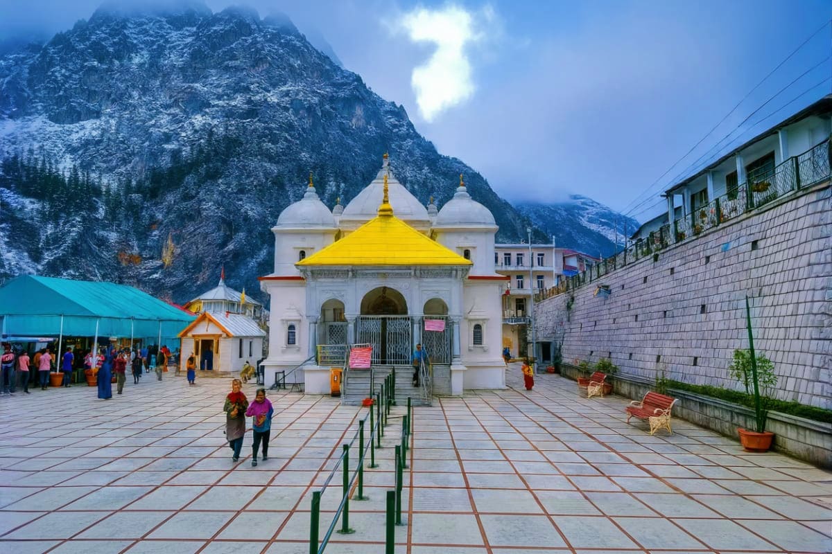 White temple with golden yellow dome in mountain valley, pilgrims walking in courtyard with snow-capped peaks in background