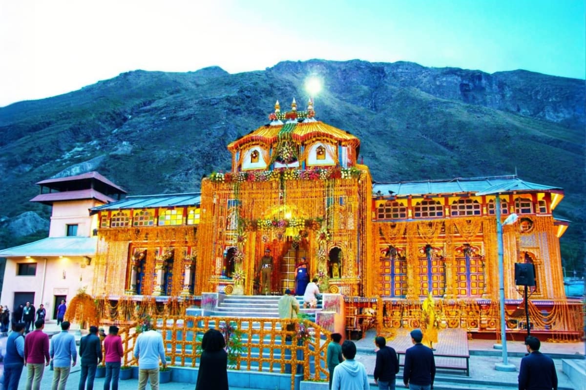 Golden temple with ornate architecture and spires nestled in mountain valley with visitors in foreground during daylight