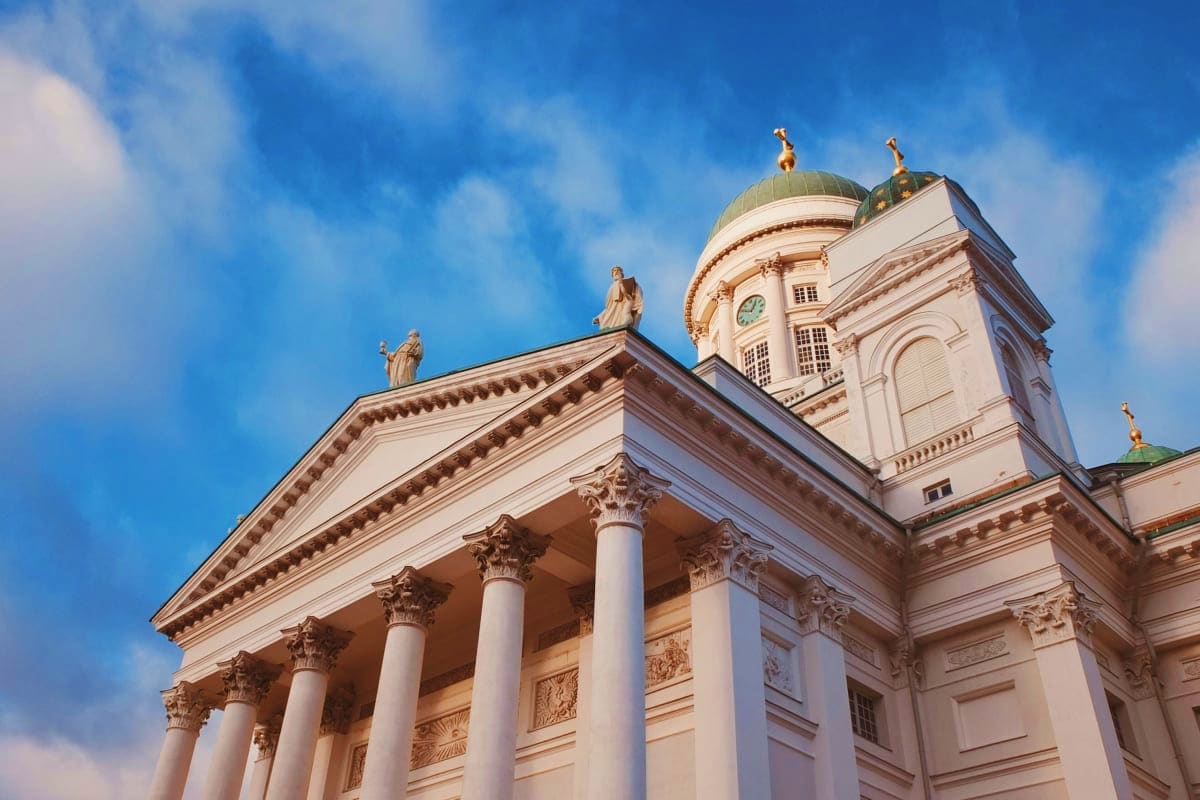 White neoclassical cathedral with golden domes and ornate columns against blue sky, Helsinki Finland landmark