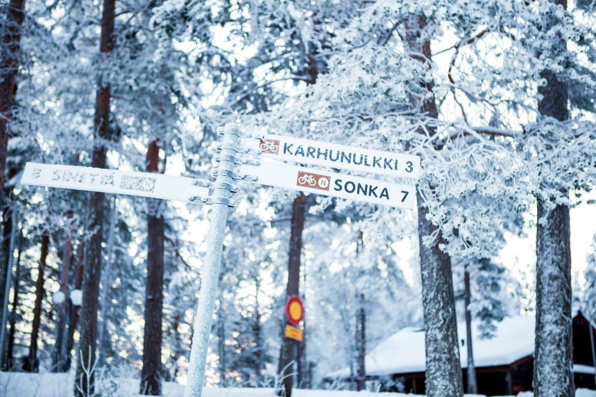 Frost-covered directional signpost in snow-laden Finnish forest showing Karhunulkki 3 and Sonka 7 trail routes
