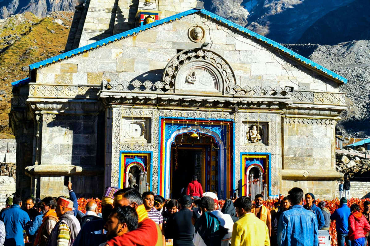 Colorful Hindu temple with bright blue trim and ornate carved details surrounded by crowds of pilgrims in mountain valley set