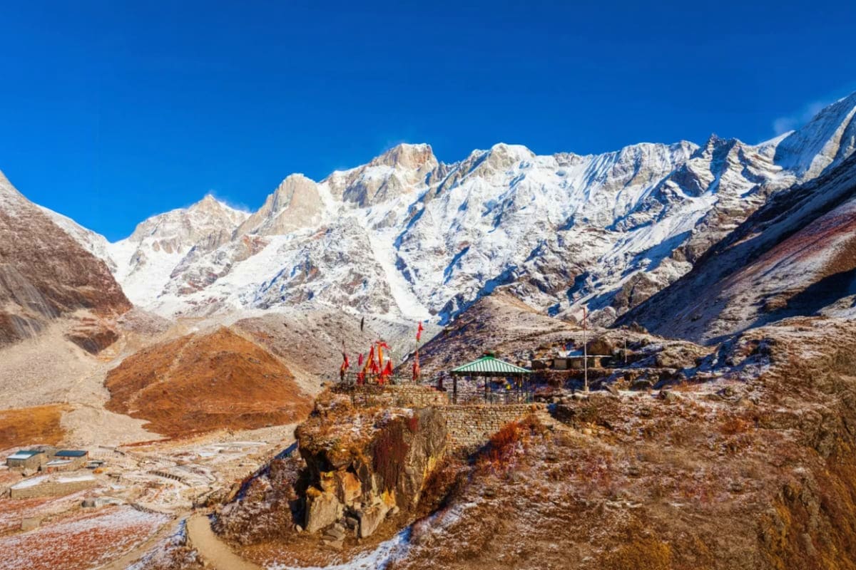 Snow-covered mountain peaks in Himalayan valley with prayer flags and temple structures at Do Dham pilgrimage site