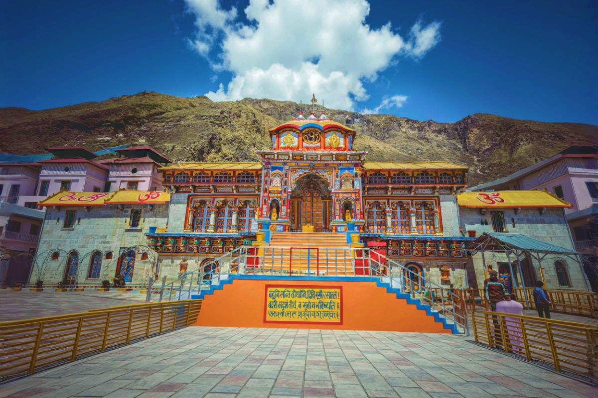 Badrinath Temple with colorful ornate facade, blue and orange steps, and snow-capped Himalayan mountains in background