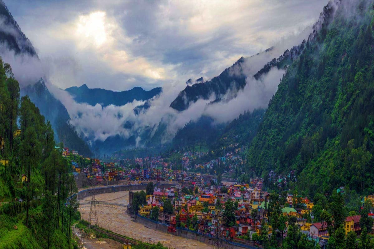 Colorful mountain town nestled in a misty valley with snow-capped peaks, a winding river, and dense evergreen forests under c