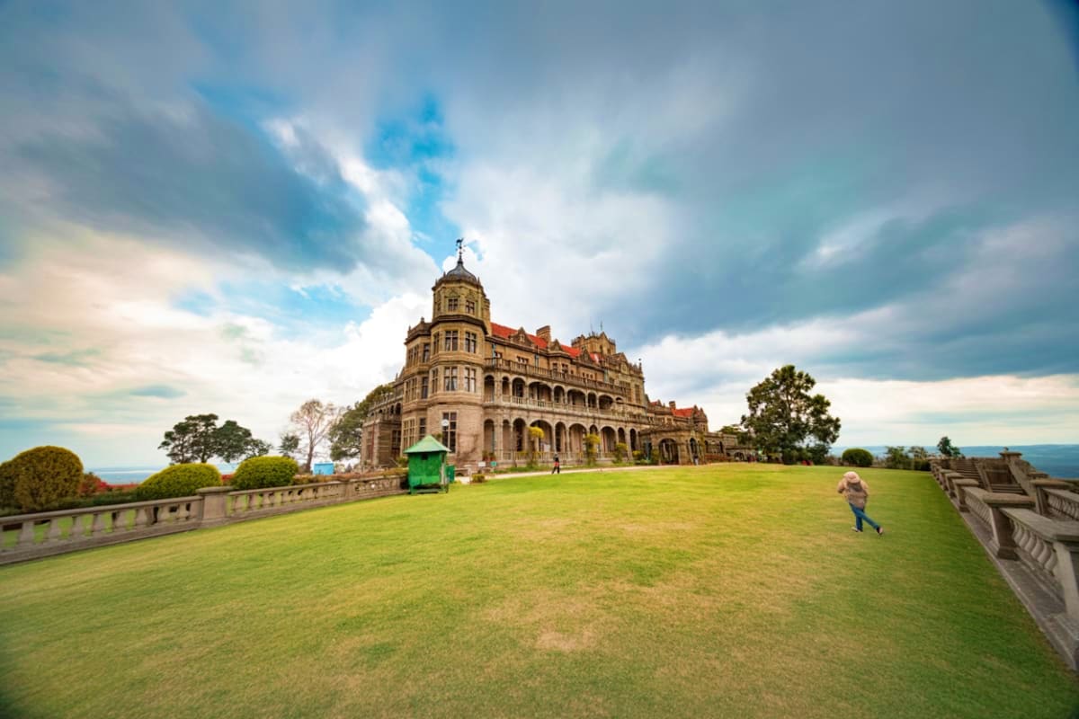 Victorian mansion on hilltop with manicured lawn, ornate architecture, and mountain views visible in background