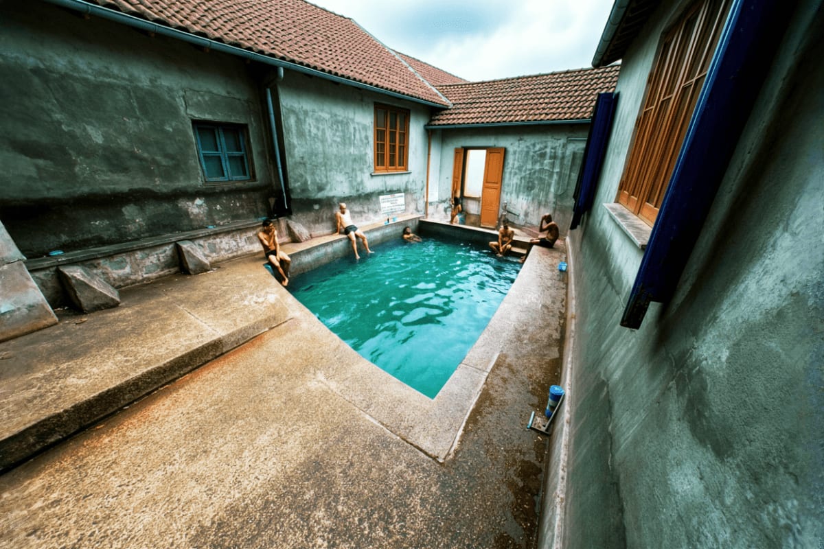 Himachal Family Explorer with Nature Temples and Snow Valleys Tourists bathing in turquoise geothermal hot spring pool surrounded by weathered concrete walls and traditional buildings wit