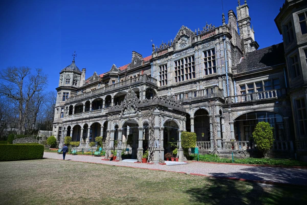 Grand Victorian mansion with ornate stone facade, multiple turrets, and manicured courtyard on clear sunny day