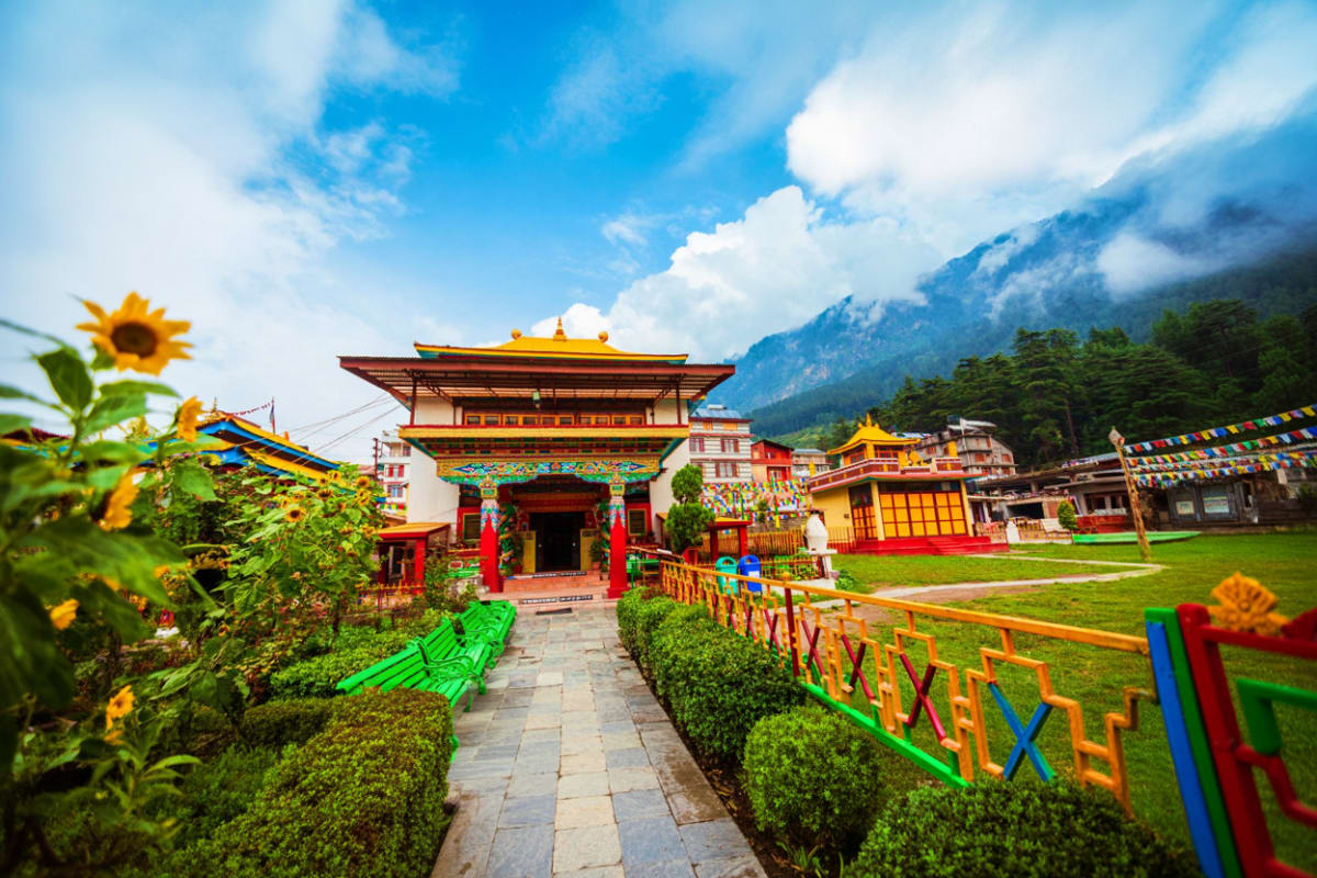 Colorful Buddhist monastery with red and gold architecture surrounded by sunflowers and green hedges, mountain valley landsca