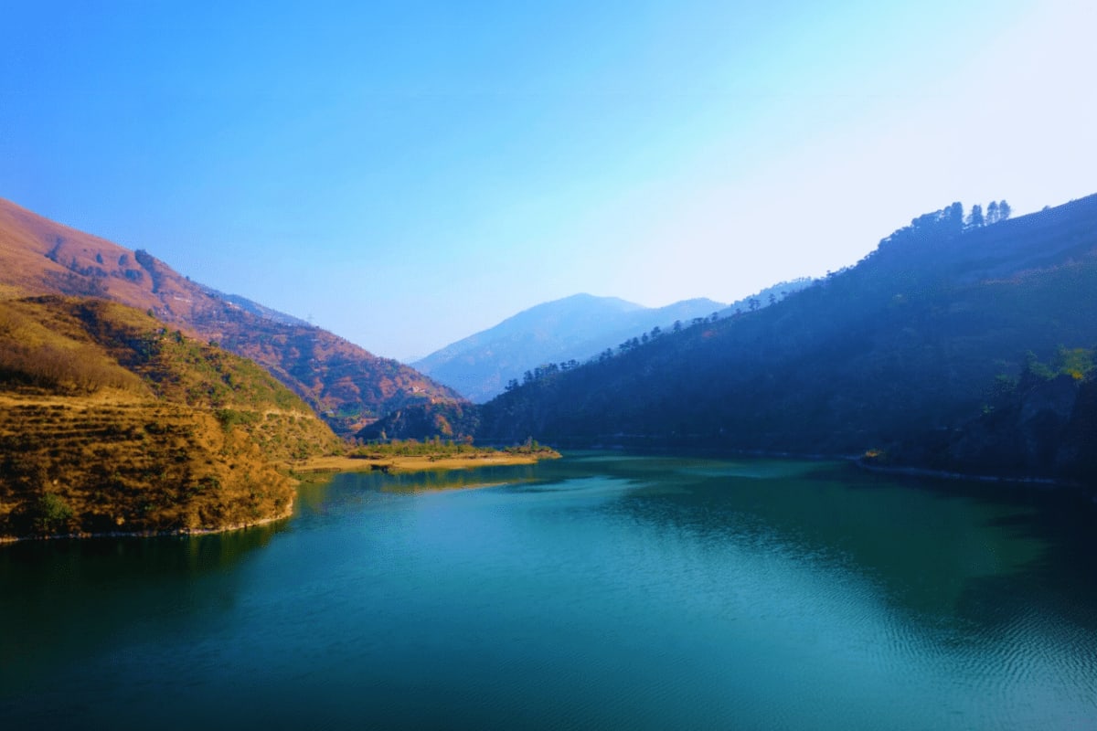 Himachal Hills Tour from Chandigarh Turquoise lake surrounded by forested mountains and golden hillsides in Himachal Pradesh under clear blue sky