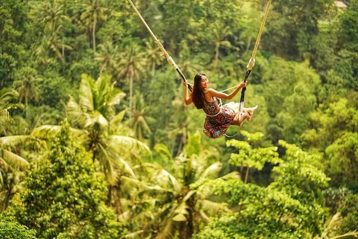 Woman swinging on rope swing over lush tropical jungle forest canopy in Bali
