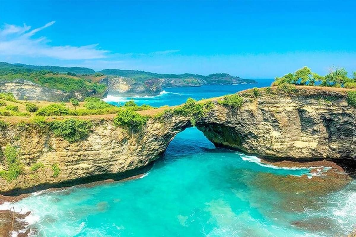 Natural rock arch bridge over turquoise ocean water with limestone cliffs and tropical vegetation at Bali coastline