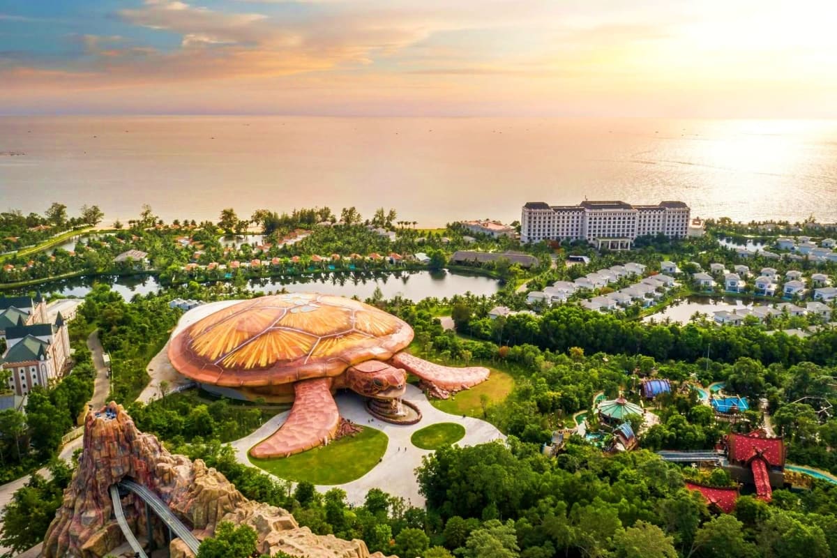 Aerial view of giant golden sea turtle sculpture at theme park with lagoon, resort hotel, and lush tropical greenery at sunse