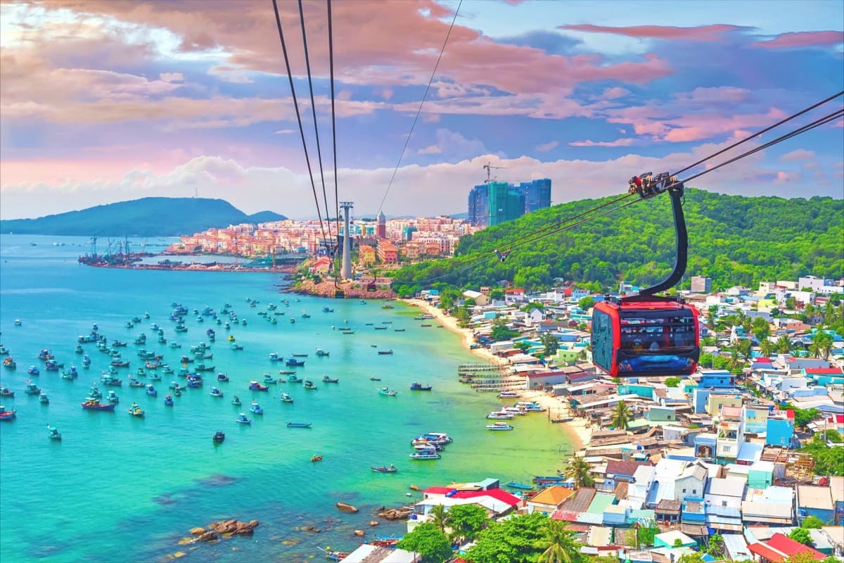 Cable car ascending above tropical coastal town with turquoise waters, fishing boats, and lush green hills at sunset