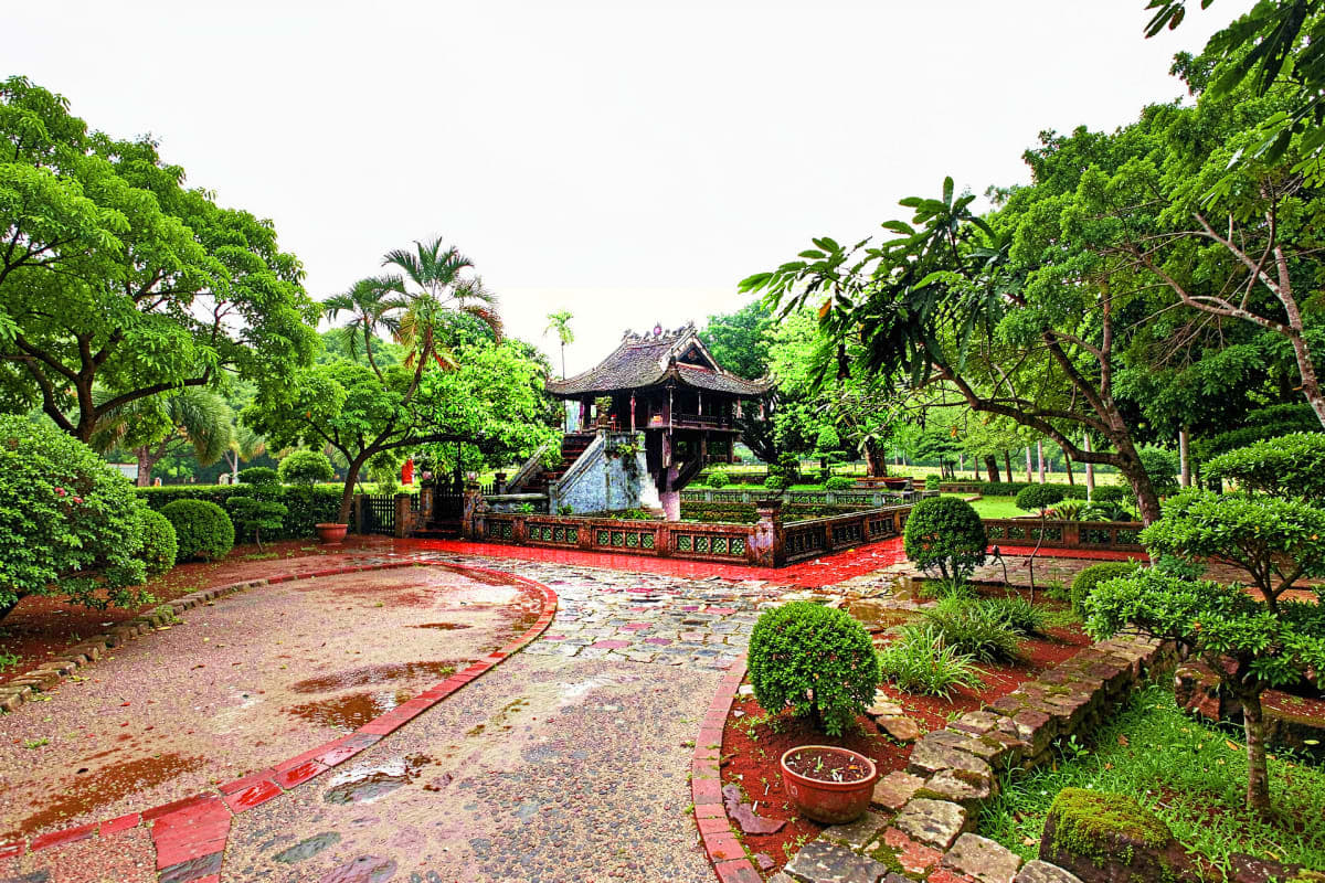 Traditional Vietnamese temple with red courtyard and wooden architecture surrounded by lush green trees and tropical vegetati