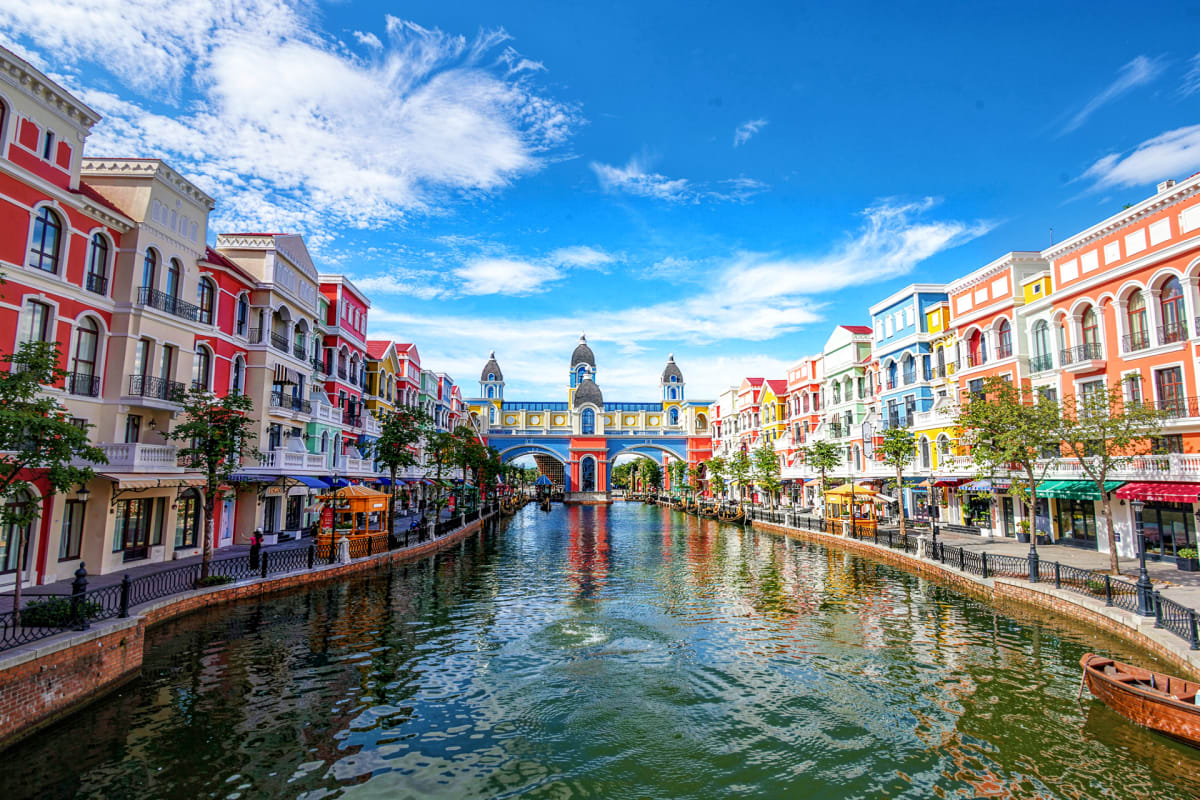 Colorful Venetian-style buildings reflected in a canal with a blue bridge and clock towers under clear blue sky at Phu Quoc t