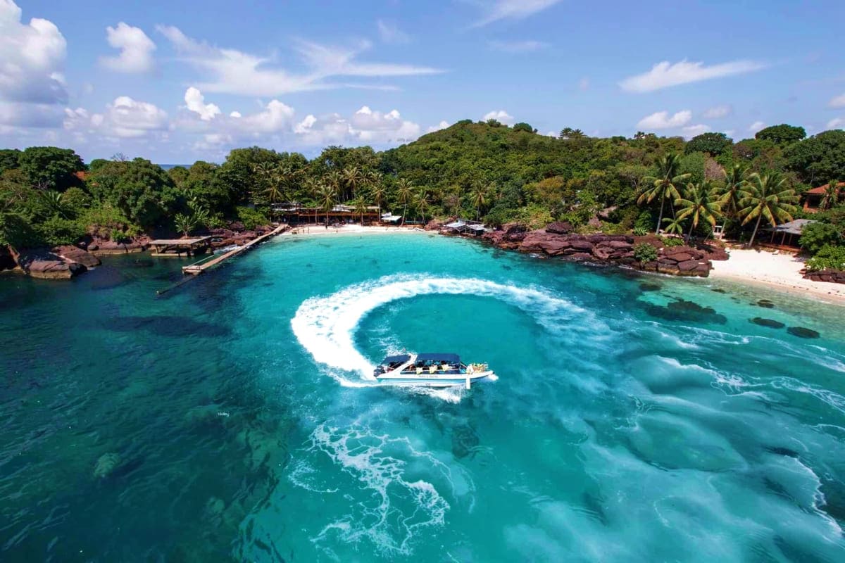 Aerial view of a speedboat creating a white wake circle in turquoise waters off Phu Quoc Island, with tropical beach and palm