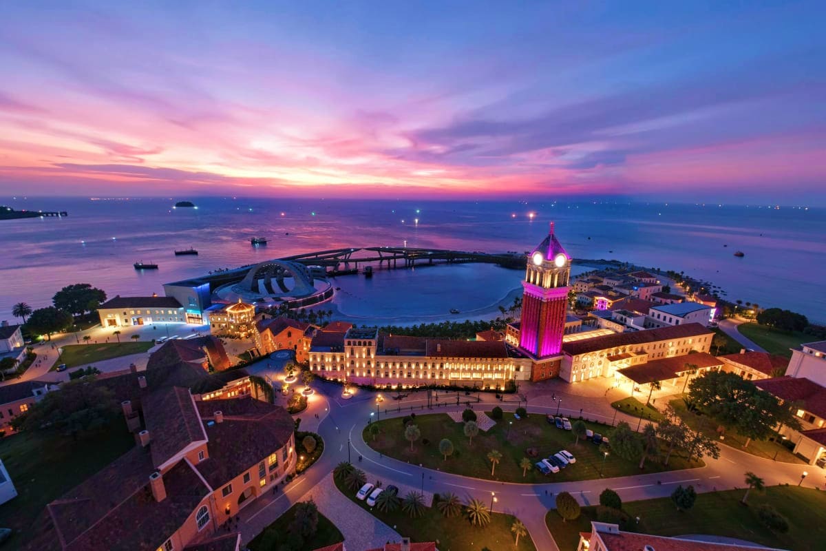 Aerial view of Phu Quoc at sunset with illuminated tower, lagoon, and coastal buildings under purple sky