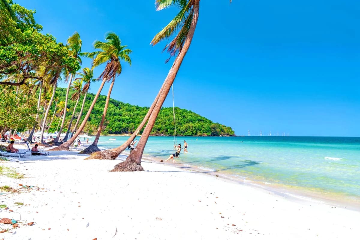 Tropical beach in Phu Quoc with palm trees, white sand, turquoise water, and tourists swimming and relaxing