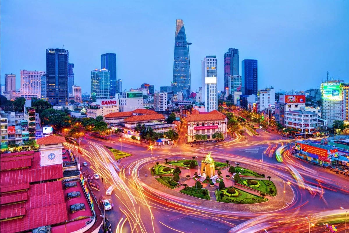 Ho Chi Minh City skyline at dusk with Bitexco Financial Tower, illuminated traffic roundabout, and colonial architecture buil