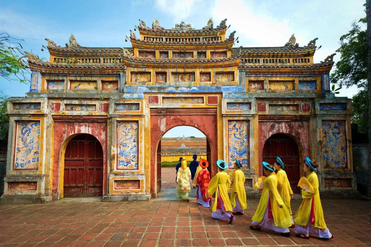 People in traditional yellow and red Vietnamese áo dài robes walking through ornate yellow and red temple gate with curved ro