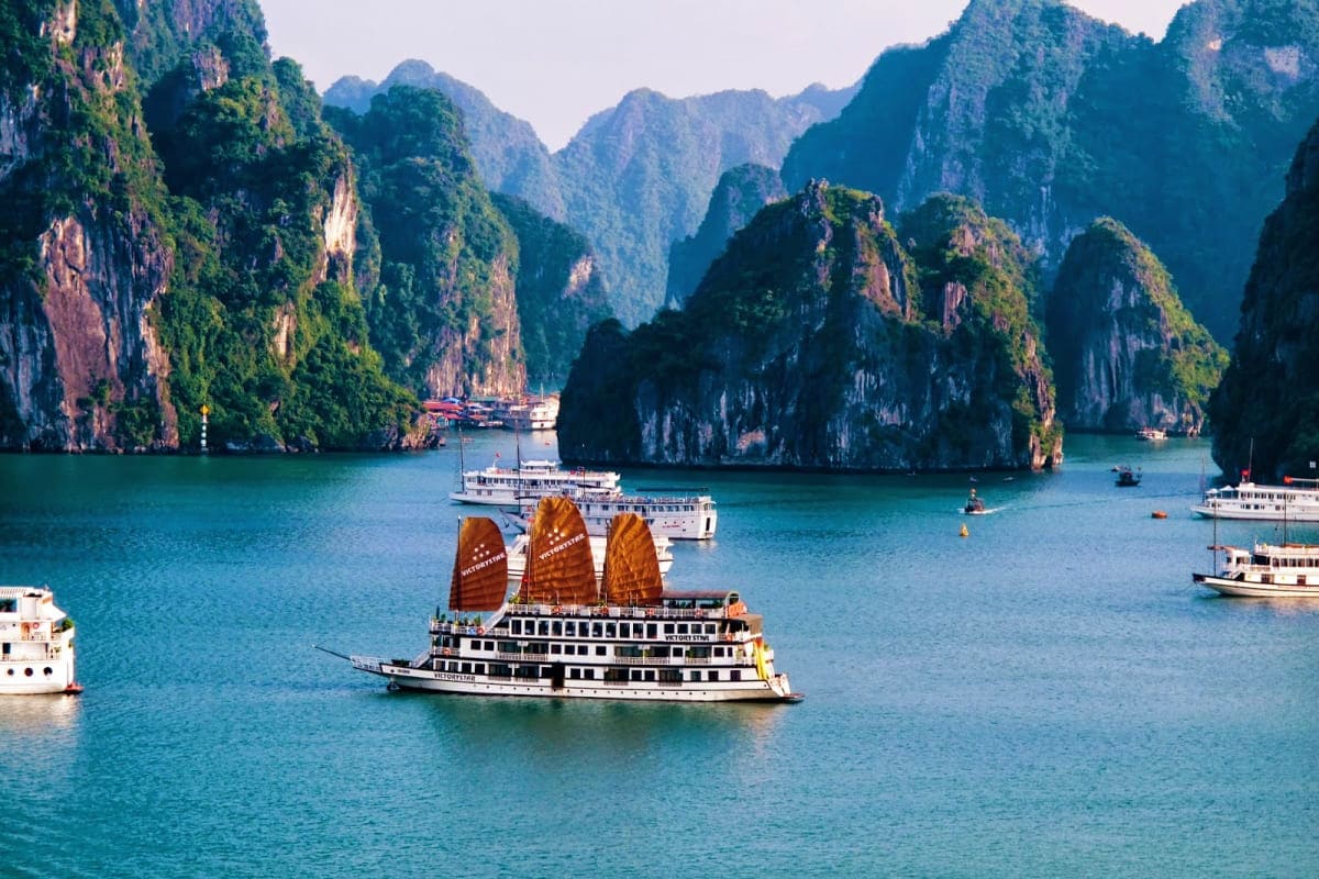 Traditional junk boat with golden sails in Halong Bay, Vietnam, surrounded by limestone karst mountains and turquoise water