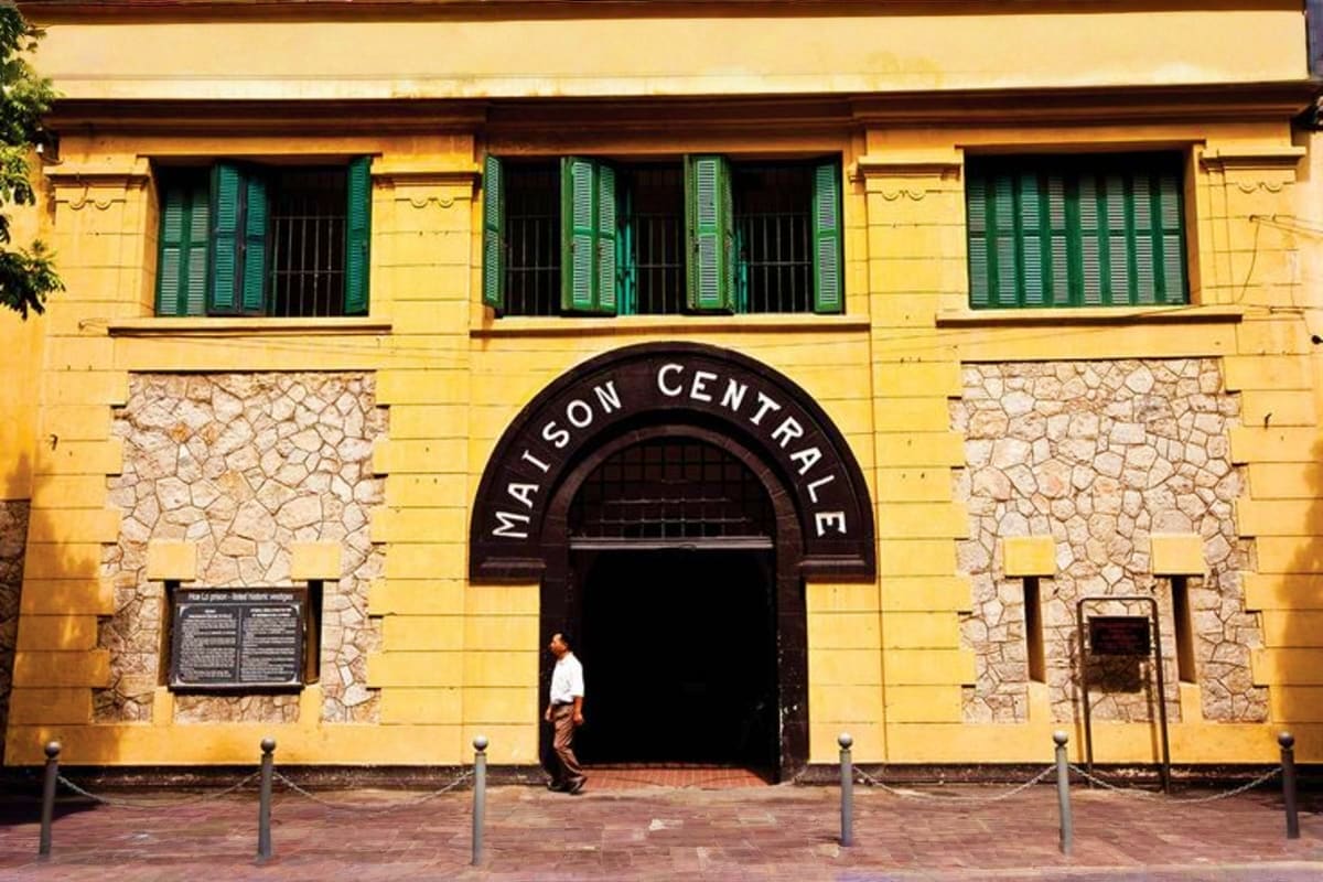 Yellow colonial building with green shuttered windows and arched "Maison Centrale" entrance, Hanoi prison historical landmark