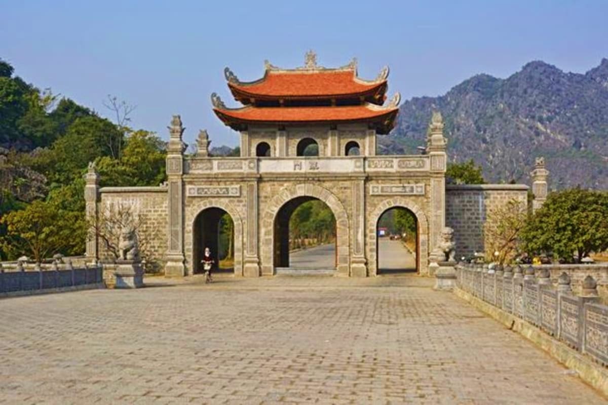 Traditional Vietnamese temple gate with orange curved roofs, stone archways, and mountains in background