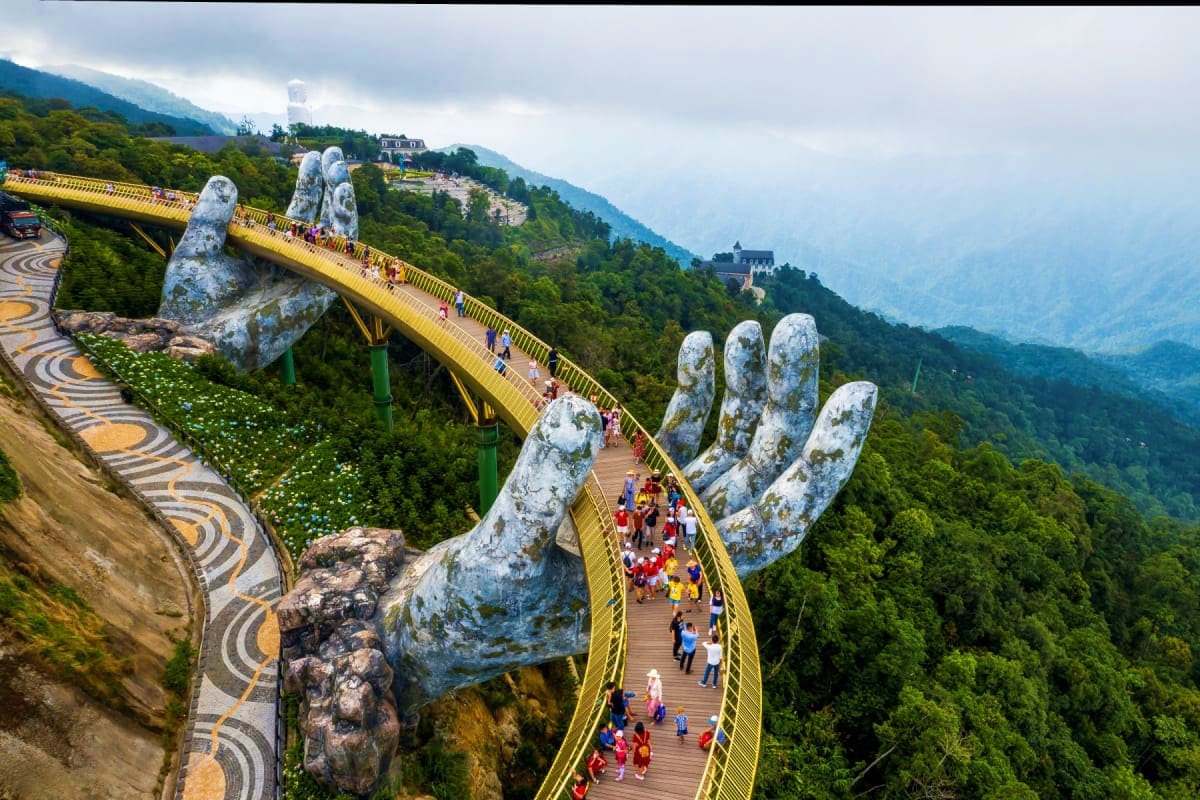 Golden Bridge held by giant stone hands at Ba Na Hills, Da Nang, Vietnam, with tourists walking and mountain landscape below