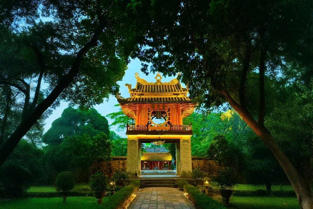 Traditional Vietnamese pagoda with golden tiled roof and red columns surrounded by lush green trees and manicured garden