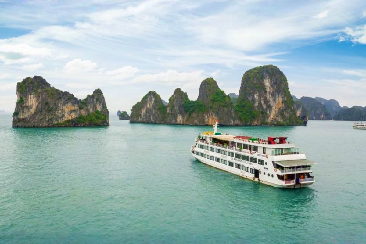 Cruise ship anchored in turquoise waters near dramatic limestone karst formations in Ha Long Bay, Vietnam