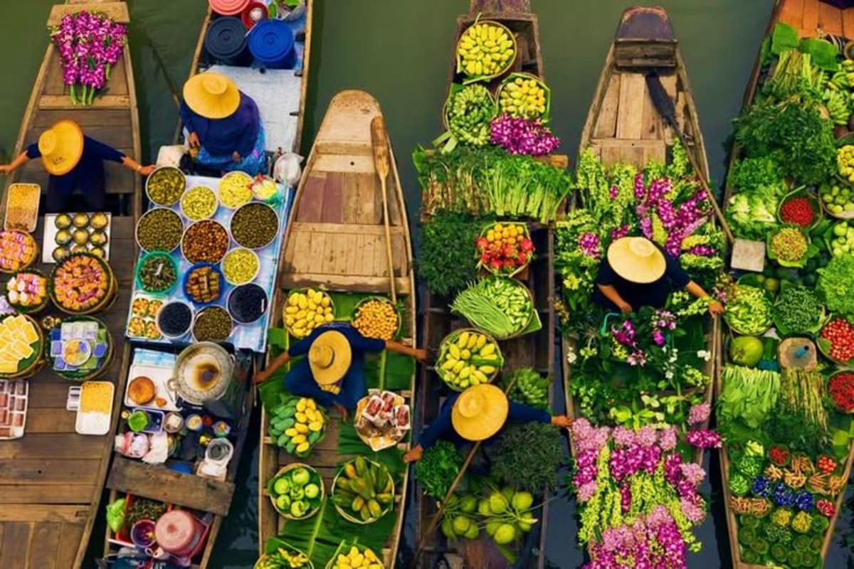 Overhead view of traditional wooden boats at a Vietnamese floating market displaying fresh produce, flowers, and prepared foo