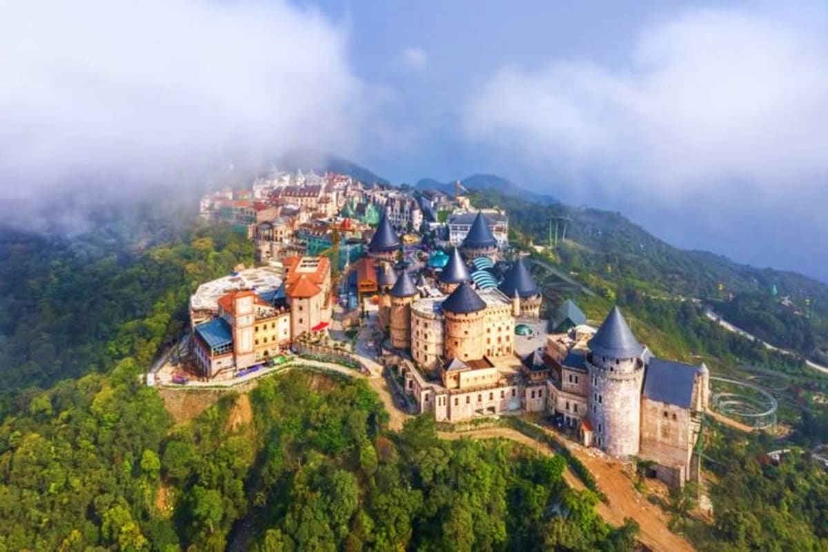 Aerial view of Neuschwanstein Castle nestled in forested mountains with mist-covered peaks and a village in the background