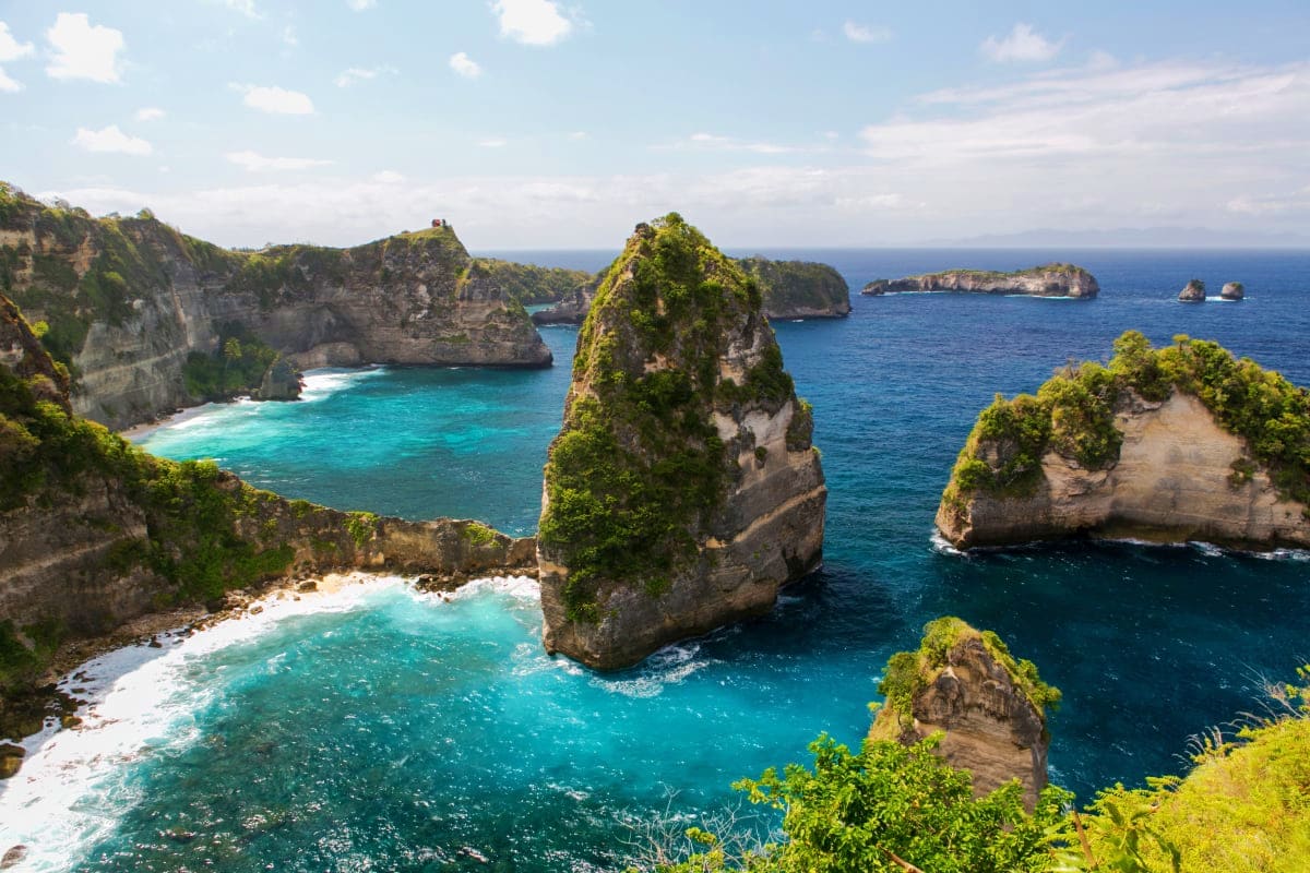 Aerial view of Kelingking Beach cliffs with turquoise water, rock formations, and lush green vegetation in Bali, Indonesia
