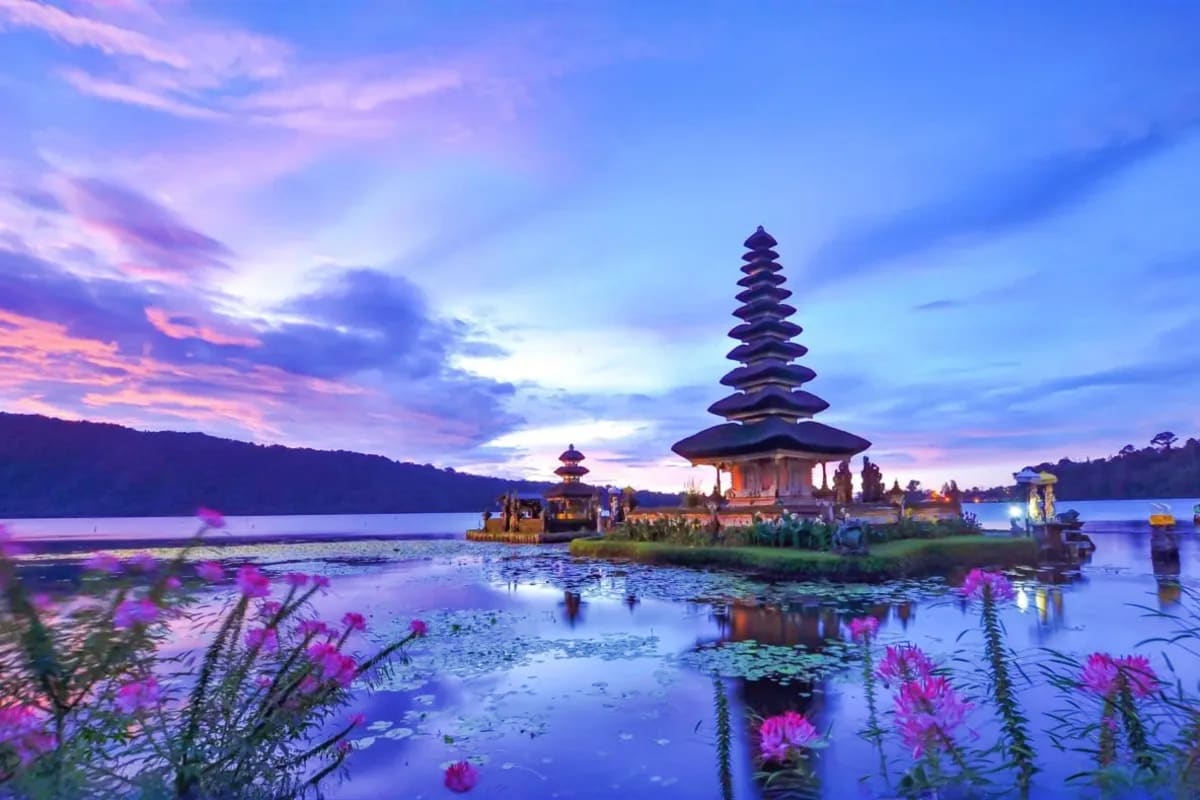 Pura Ulun Danu temple at sunset in Bali with pink water lilies, reflected in Lake Bratan at dusk with purple sky