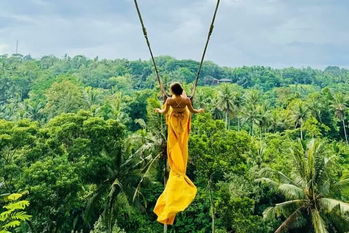 Woman in yellow dress on jungle swing overlooking Bali rainforest with palm trees and dense tropical vegetation