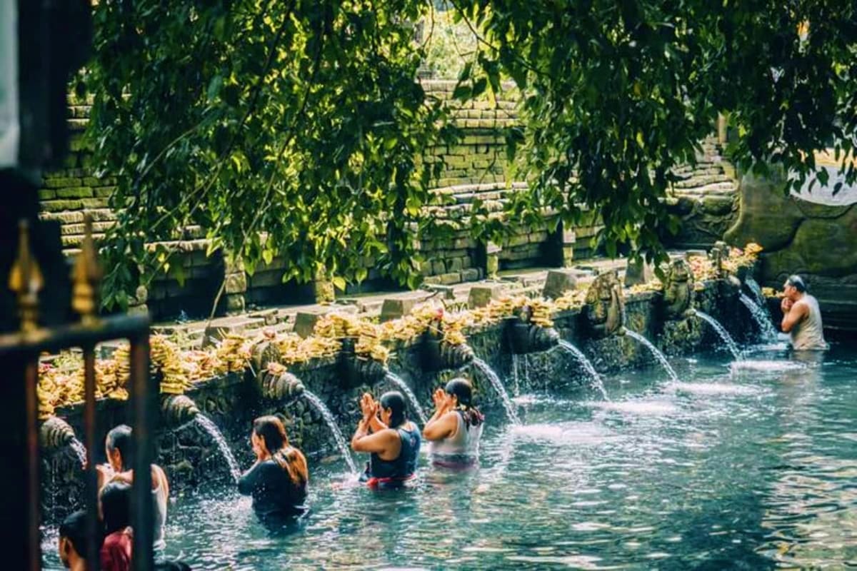 Tourists bathing in clear water at Tirta Empul temple's sacred spring pools in Bali, surrounded by lush green vegetation and 