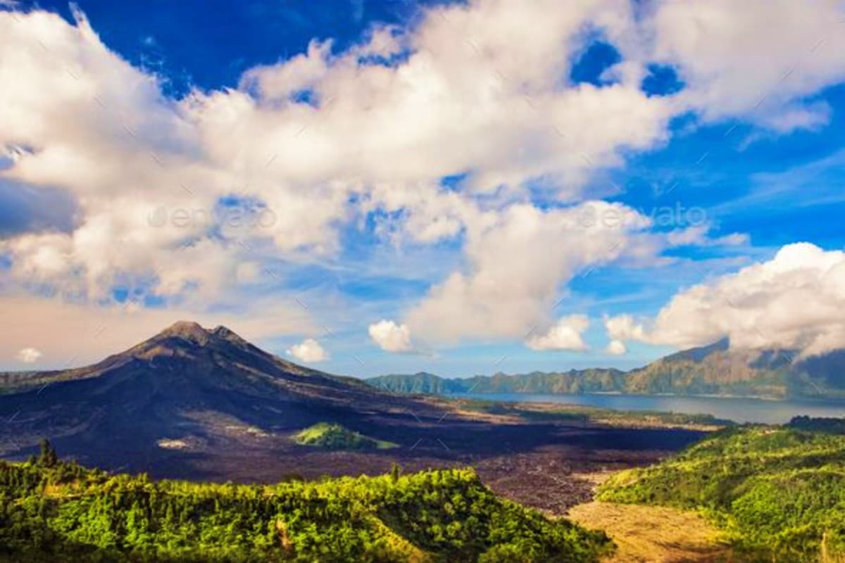 Volcanic landscape in Bali with Mount Agung, forested slopes, crater lake, and cloudy blue sky