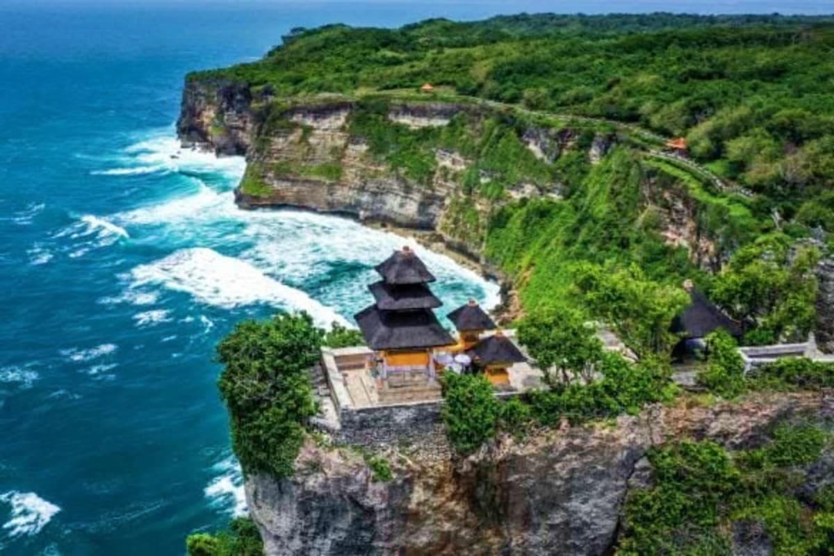 Clifftop temple with black pagoda roofs overlooking turquoise ocean waves and dramatic rocky coastline with lush green vegeta