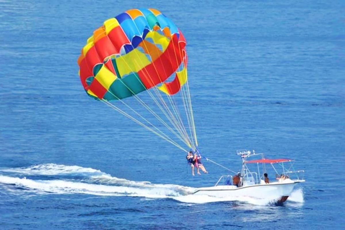 Two people parasailing behind a white boat with colorful rainbow parachute over blue ocean water and waves