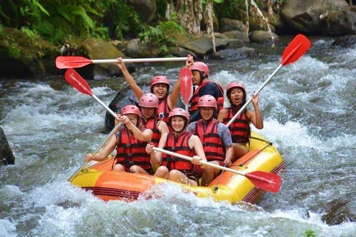Group of tourists white water rafting on rapids in Bali river wearing pink helmets and life jackets in inflatable raft
