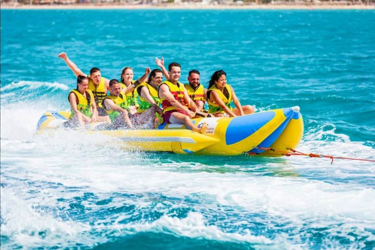 Group of people riding yellow and blue banana boat in turquoise ocean waves at tropical beach