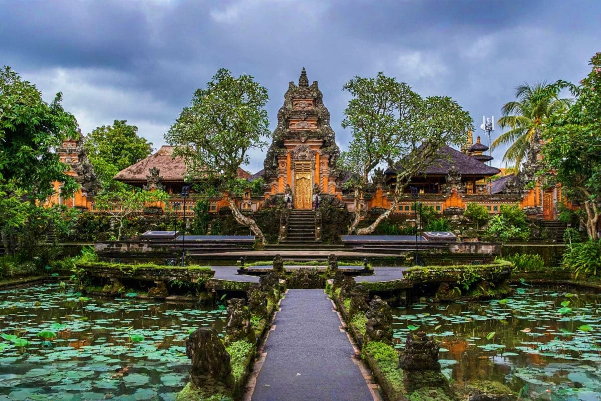 Ancient Hindu temple with tiered stone tower, yellow gates, and manicured gardens reflected in lily pond surrounded by tropic