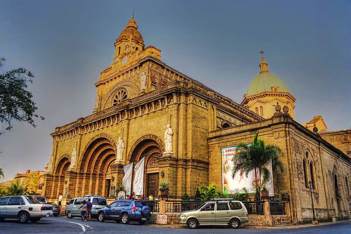 Ultimate Manila and Cebu Holiday Package Historic yellow stone cathedral with ornate dome and green cupola, parked cars, and tropical plants in front