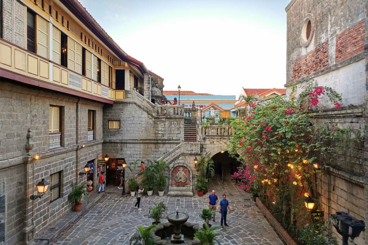 Ultimate Manila and Cebu Holiday Package Historic stone courtyard in Manila with colonial architecture, blooming bougainvillea, fountain, and ocean view