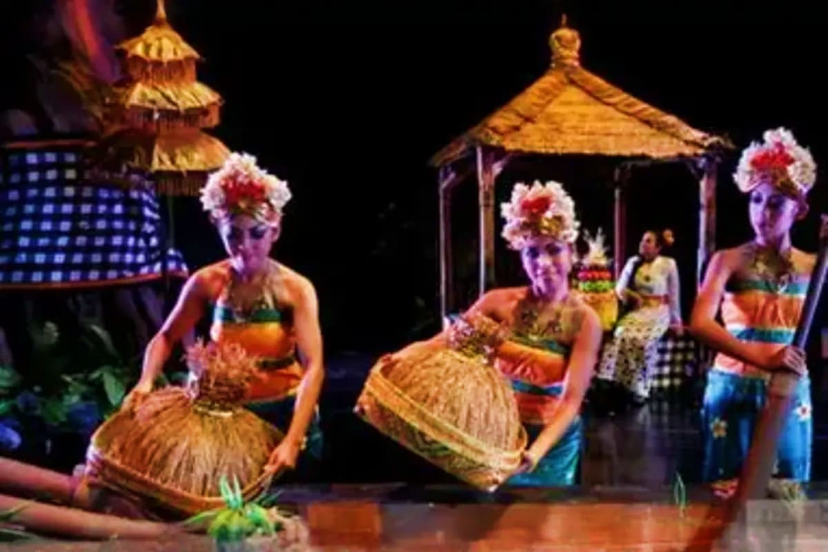 Performers in traditional Balinese costumes and colorful grass skirts dancing on stage with golden temple structures and tiki